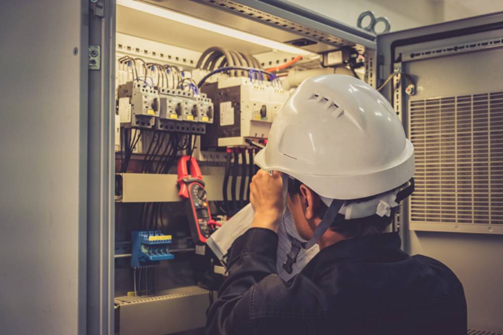 A man in a hard hat and white shirt diligently works on electrical installation.